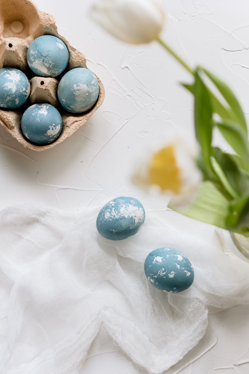 blue easter eggs beside vase with white tulips